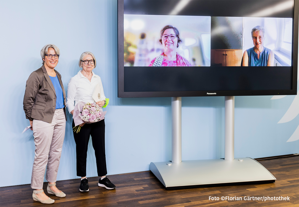 Kerstin Claus und Barbara Kavemann stehen neben einem Videobildschirm, auf dem Julia Gebrande und Silke Gahleitner zu sehen sind