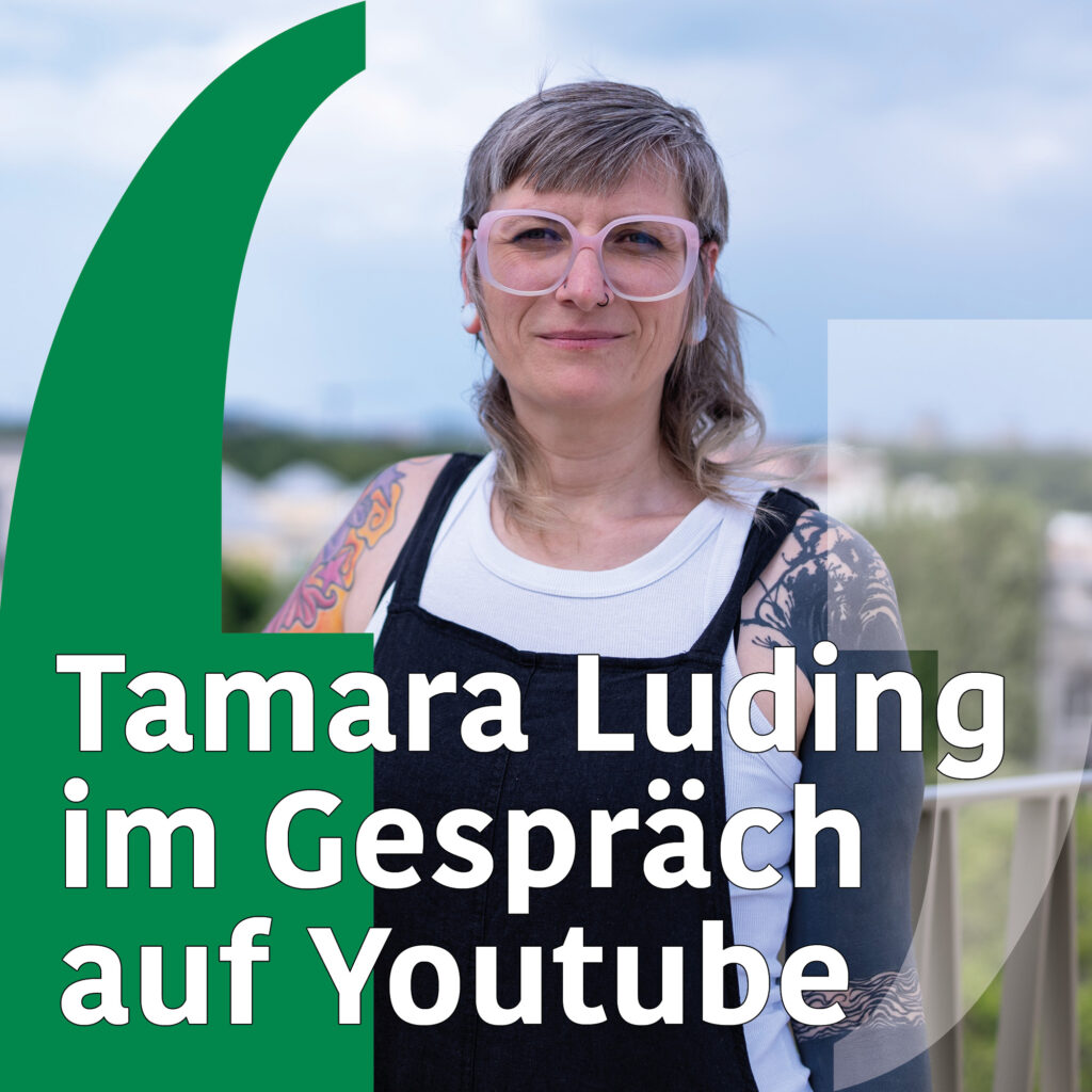 Foto einer Frau mit vorne kurzen hinten langen grauen Haaren und großer rosa Brille. Sie hat mehrere Tattoos auf den Armen und trägt eine Latzhose. Text: "Tamara Luding im Gespräch auf Youtube"