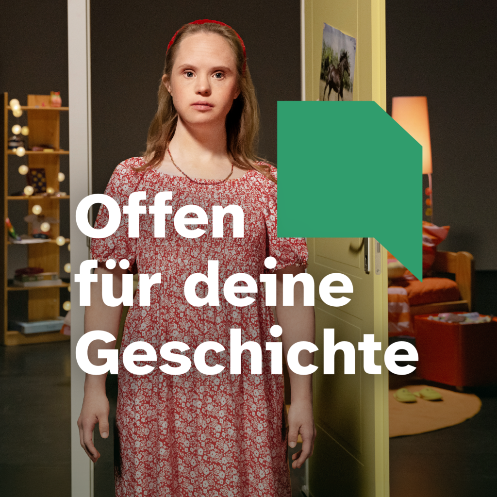 Motiv der Kampagne "Offen für deine Geschichte": Eine junge Frau mit Down-Syndrom steht im Zentrum des Fotos. Sie ist blond und hat ein rot-weiß geblümtes Kleid an. Im Hintergrund eine Theaterkulisse mit geöffneter Gelber Tür. Dahinter ist die Einrichtung eines Kinderzimmers zu erkennen. Darauf Text: "Offen für deine Geschichte" und Logo offene Tür