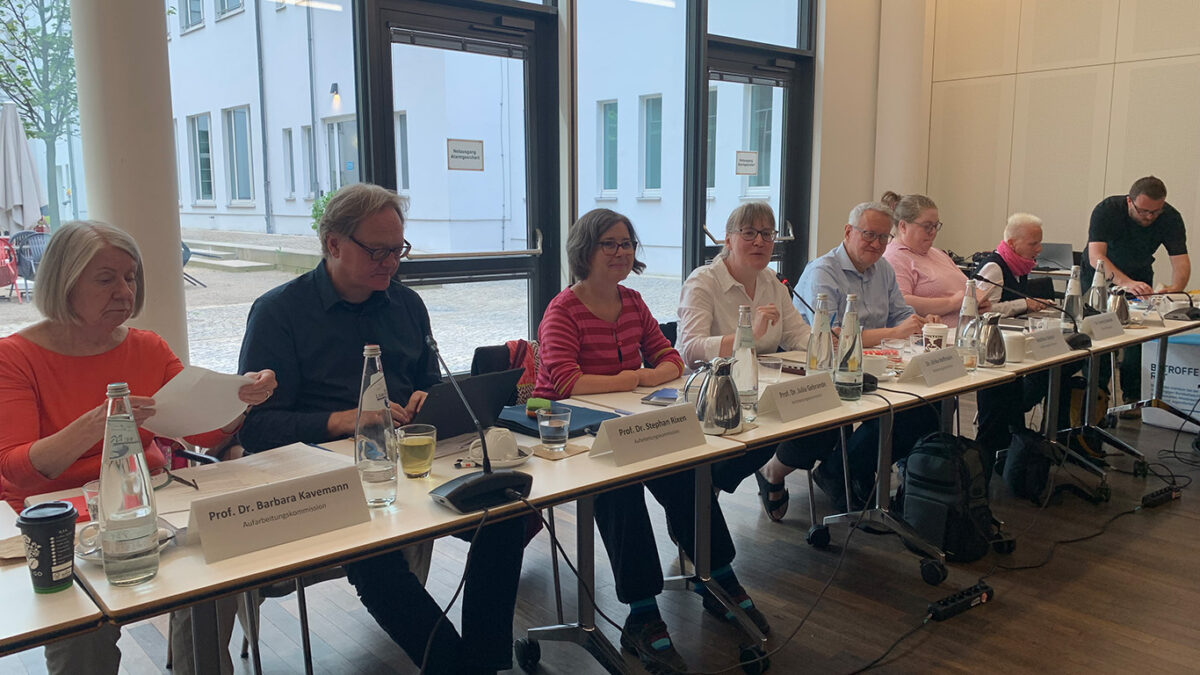 Ein Konferenztisch mit Namensschildern, dahinter von links nach rechts Barbara Kavemann, Stephan Rixen, Julia Gebrande, Ulrike Hoffmann, Matthias Katsch und Gäste der Kommission